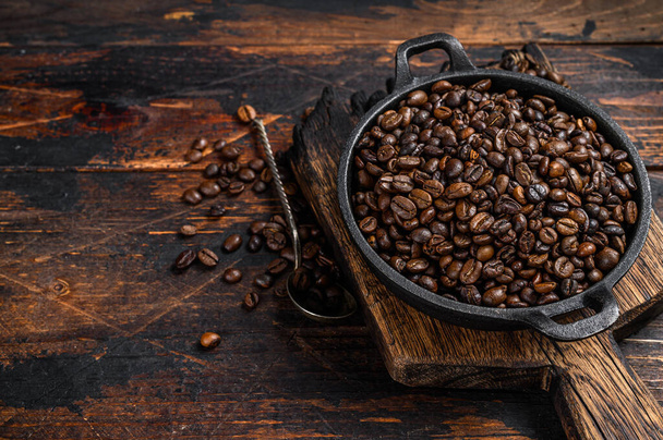 Dark roasted Coffee beans in a pan. Dark wooden background. Top view. Copy space - Photo, Image