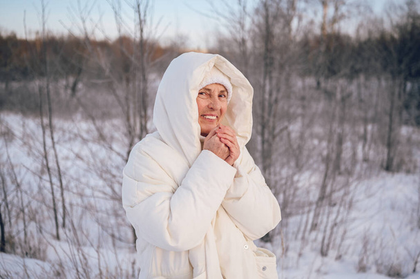 Gelukkig oudere oudere volwassen vrouw in witte warme outwear spelen met sneeuw in de zonnige winter buiten. Gepensioneerden gezonde mensen vakantie winteractiviteiten, actieve levensstijl concept - Foto, afbeelding