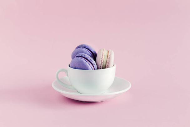 Tasse mit französischen Macarons auf rosa Pastellgrund. Rosa und violette Macarons. Platz für Text. - Foto, Bild