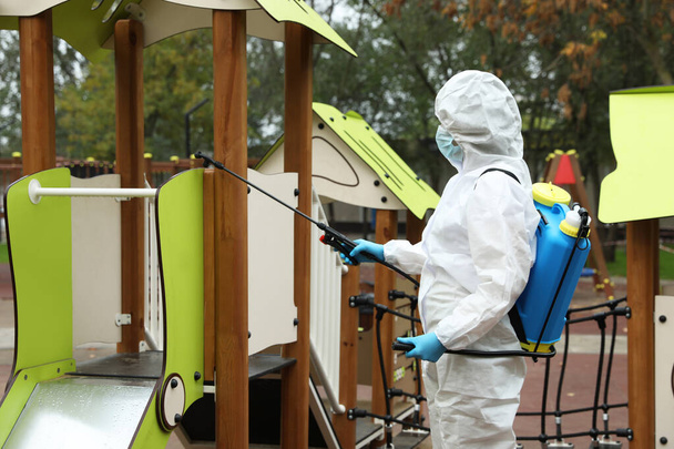 Woman wearing chemical protective suit with disinfectant sprayer on playground. Preventive measure during coronavirus pandemic - Φωτογραφία, εικόνα