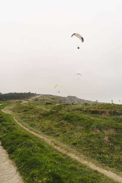 Paragliding over the green cliffs on an overcast day - Valokuva, kuva