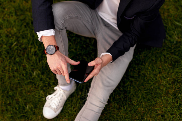 Stylish man sitting on grass and using smartphone - Photo, Image
