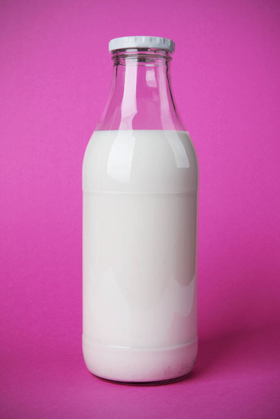 Καλό πρωινό με ένα γυάλινο μπουκάλι γεμάτο φρέσκο γάλα. Το ασβέστιο κάνει καλό στην υγεία. Φωτογραφία σε ροζ φόντο με σκιά - Φωτογραφία, εικόνα