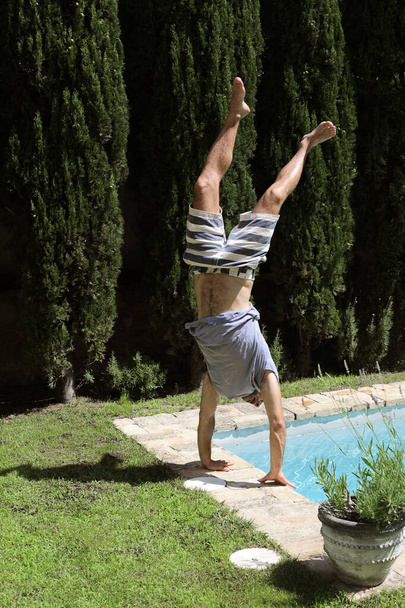 Male wearing t-shirt and swimsuit doing a handstand on poolside - Foto, afbeelding
