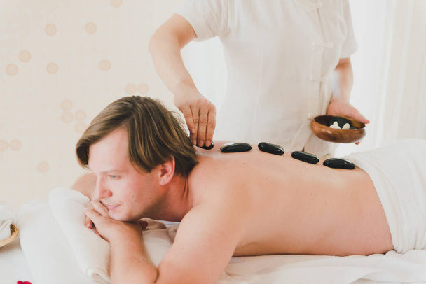 A young man is happy and relaxed with a hot stone therapy in the spa. - Valokuva, kuva
