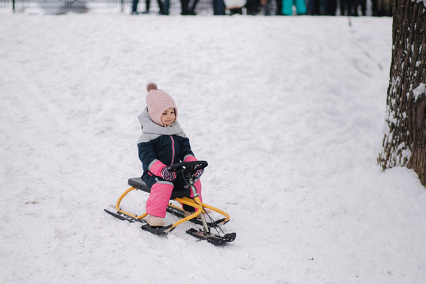 Маленька дівчинка насолоджується катанням на санях. Дитячий слайд. Діти катаються в парку взимку. Розваги на відкритому повітрі для сімейних різдвяних канікул
 - Фото, зображення