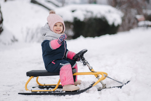 Little girl enjoy a sleigh ride. Kid sledding. Kids sled in park in winter. Outdoor fun for family Christmas vacation - Foto, imagen