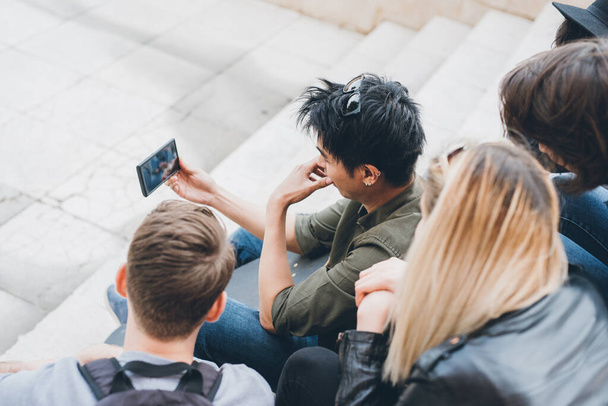 Grupo de amigos multiétnicos millennials usando teléfonos inteligentes adictos a las tendencias tecnológicas siguiendo y charlando y viendo videos - Foto, Imagen