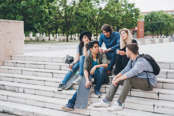 Група з чотирьох фігуристів багатоетнічні кращі друзі, що сидять на відкритому повітрі, веселяться плітки, спілкуються і сміються
 - Фото, зображення