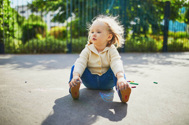 Thoughtful adorable toddler girl sitting on the ground on a street - Фото, изображение