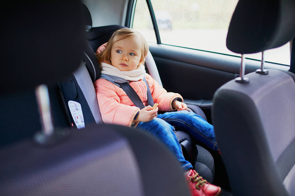 Adorable toddler girl in modern car seat eating cookie. Little kid traveling by car. Child safety on the road. Trip with a baby - Fotografie, Obrázek