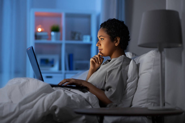 woman with laptop in bed at home at night - Foto, afbeelding