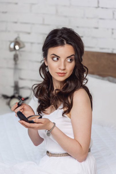 woman applying make-up while sitting on bed at the hotel room - Foto, Bild