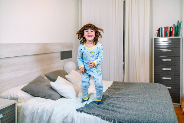 bambino molto felice saltando sul letto con il pigiama prima di andare a letto - Foto, immagini