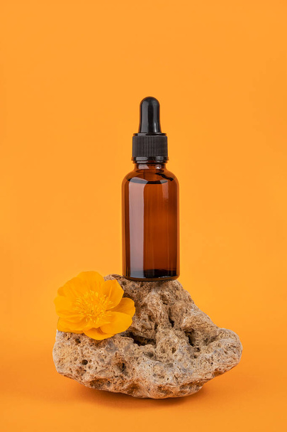 Serum or essential oil in brown glass bottle with pipette on stone and flowers on orange background. Natural Organic Spa Cosmetic concept Front view. - Fotoğraf, Görsel