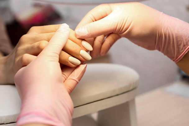 A manicure olha para a mão e examina as unhas dos clientes. O processo de manicure e cuidados com as unhas. - Foto, Imagem