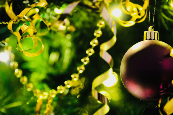 Kerstversiering, zilveren en paarse kerstballen hangend aan een kerstboom met gouden kettingen en rood en goud gedraaid lint. Een feestelijke kerst achtergrond scène - Foto, afbeelding