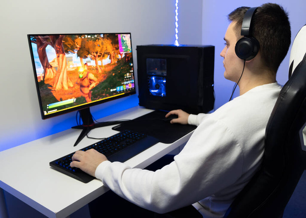 Hän pelaa nettipeliä. Pelaaja istuu tietokoneella sinisessä neonhuoneessa. - Valokuva, kuva