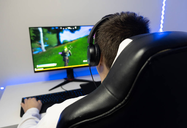 Hän pelaa nettipeliä. Pelaaja istuu tietokoneella sinisessä neonhuoneessa. - Valokuva, kuva