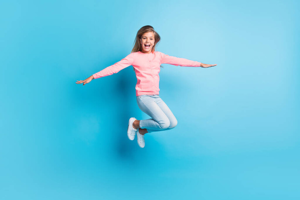 Photo portrait of girl making plane with hands jumping up isolated on pastel blue colored background - Fotó, kép