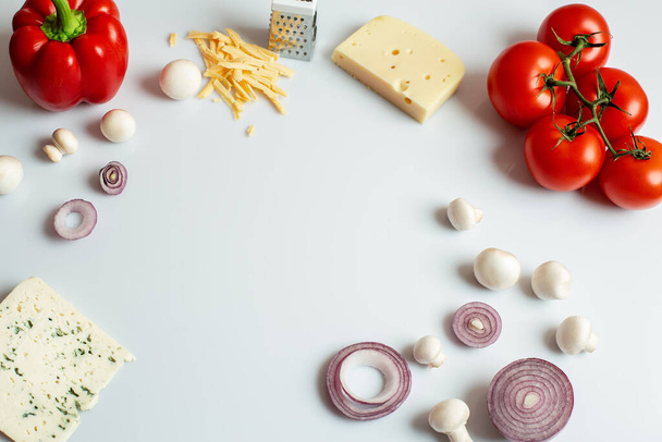 Zutaten für hausgemachte Pizza auf weißem Hintergrund. Zubereitungserzeugnisse: Tomaten, Paprika, Pilze, Käse, Zwiebeln. Draufsicht mit Kopierraum auf weißem Hintergrund. Nahaufnahme. - Foto, Bild