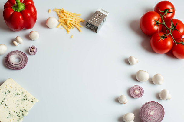 Zutaten für hausgemachte Pizza auf weißem Hintergrund. Zubereitungserzeugnisse: Tomaten, Paprika, Pilze, Käse, Zwiebeln. Draufsicht mit Kopierraum auf weißem Hintergrund. Nahaufnahme. - Foto, Bild
