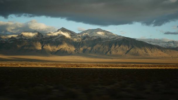 Road trip, driving auto from Death Valley to Las Vegas, Nevada USA. Hitchhiking traveling in America. Highway journey, dramatic atmosphere, sunset mountain and Mojave desert wilderness. View from car - Photo, Image