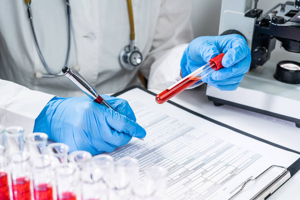 Blood test tubes. Senior female scientist examining blood test tubes at her laboratory dna testing - Foto, afbeelding