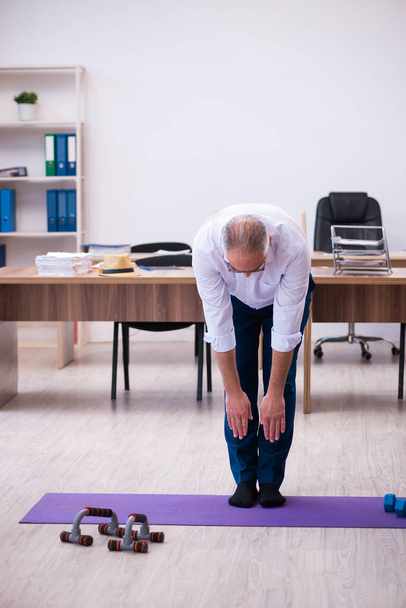 Vieil homme d'affaires employé faisant des exercices sportifs dans le bureau - Photo, image