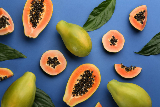 Fresh ripe papaya fruits with green leaves on blue background, flat lay - Фото, зображення