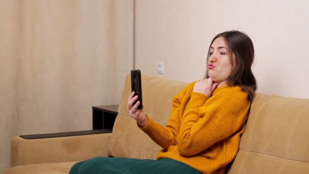 Radosna kobieta blogger w sweter grimaces siedzi na kanapie - Materiał filmowy, wideo