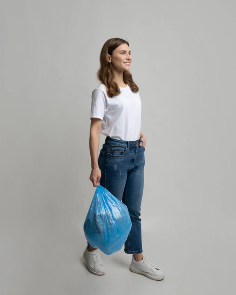 Smiling Young Lady Walking With Garbage Bag In Hands Over Gray Background - Fotoğraf, Görsel
