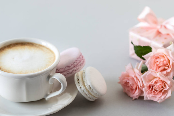 Kuppi kahvia, pastaa kakkuun, lahja laatikossa ja vaaleanpunaisia ruusuja harmaalla taustalla. Kopioi tila. - Valokuva, kuva