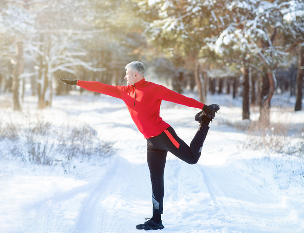 Longitud completa del hombre maduro en ropa deportiva que se calienta antes de correr al aire libre en el día de invierno nevado. Estilo de vida saludable - Foto, Imagen