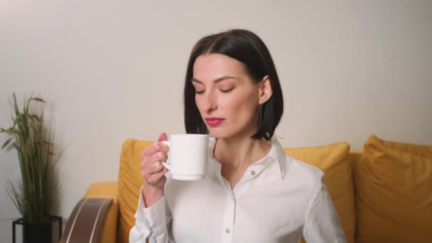 Tyytyväinen liikenainen juo teetä toimistossa. Houkutteleva nainen nauttii kupin kahvia kotona hidastettuna. Hymyilevä nainen pitelee teekuppia kädessään aamulla. - Materiaali, video