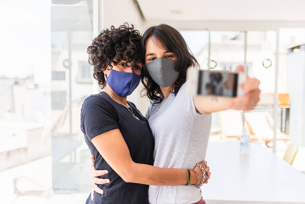 Foto stock de casal lésbico feliz usando máscara facial devido a covid19 tirar foto em casa. - Foto, Imagem