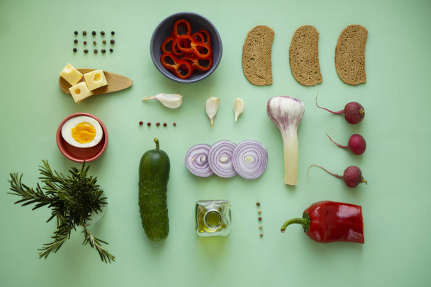 Geometric composition on a green background with products for a vegetarian breakfast. Dry bread, cheese, onions and greens for a light snack or for menu  - Photo, Image