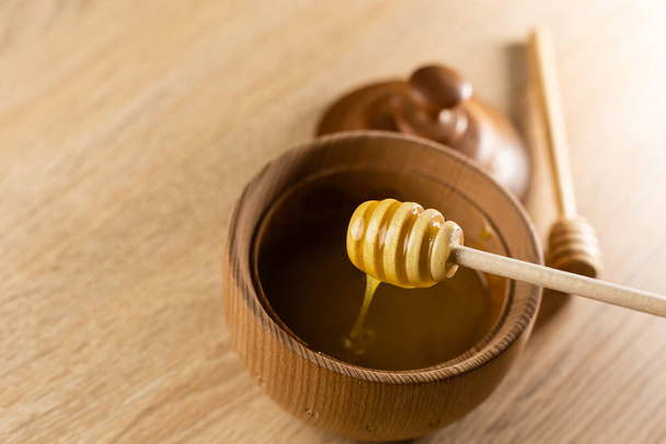 Honey with wooden honey dipper in wooden bowl on wooden table - Valokuva, kuva