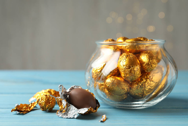 Chocolate eggs wrapped in golden foil on light blue wooden table. Space for text - Fotó, kép