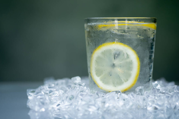 Ein Glas kühles Wasser mit Zitronenscheibe im Inneren, serviert auf einem Eiswürfelstück aus Kunstkristall - Foto, Bild