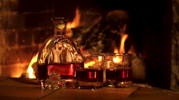 Bottiglia e bicchieri con whisky o cognac sullo sfondo del fuoco nel camino - Filmati, video