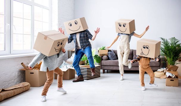 Zorgeloze ouders en kinderen in kartonnen dozen op hoofden dansen in nieuwe ruime flat terwijl plezier hebben en genieten van de verhuizing samen - Foto, afbeelding