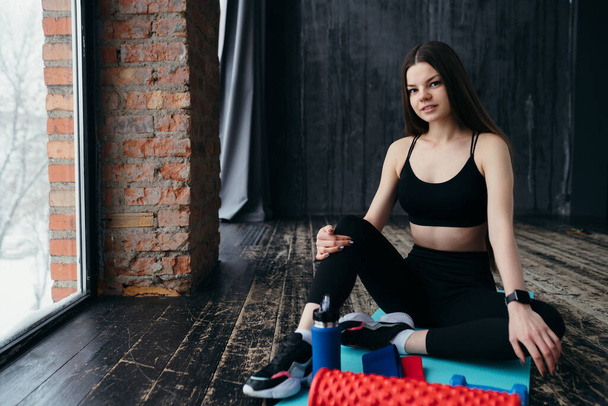 Caucasian girl in sportswear in sneakers sitting on the mat preparing for a workout - Foto, Imagen