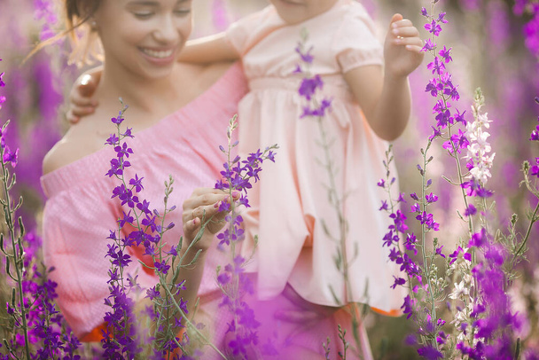 Young beautiful mother and her little daughter outdoors with flowers. Violet field of flowers and people there - Photo, Image