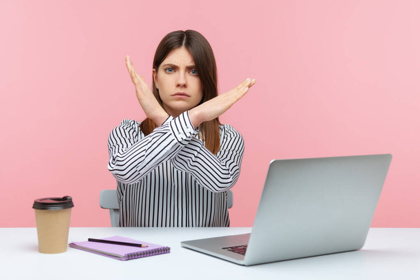 Upset bossy woman office worker sitting at workplace crossing hands showing x sign, rejecting and finishing sexual harassment at work. Indoor studio shot isolated on pink background - Foto, immagini