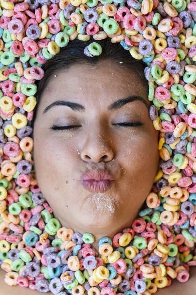 Una hermosa joven modelo hispana está cubierta de cereales para el desayuno solo mostrando su cara - Foto, imagen