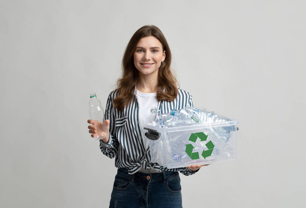 Пластиковая переработка. Улыбающаяся молодая женщина собирает бутылки для переработки отходов в контейнер - Фото, изображение