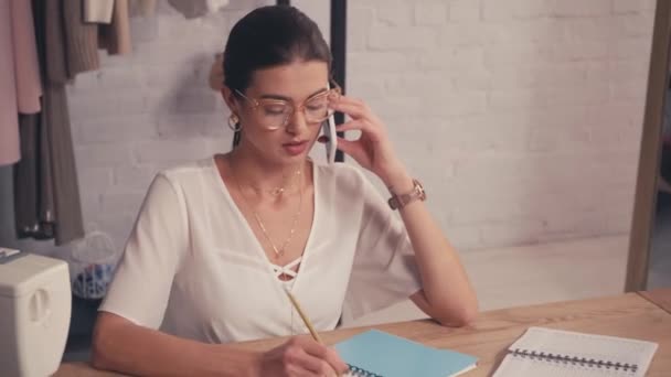 Designer in gesprek op smartphone in de buurt van notebooks en naaimachine  - Video