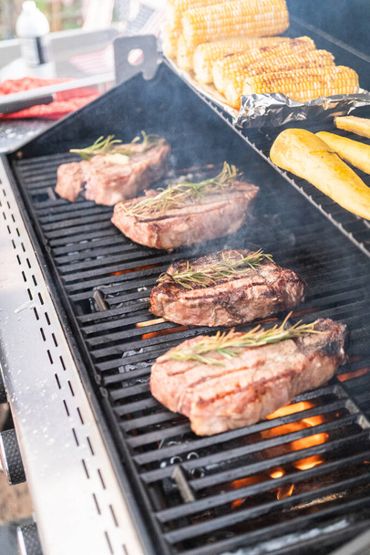 Grillen von New Yorker Steak mit einer Scheibe Butter und Rosmarin auf einem Gasgrill im Freien. - Foto, Bild