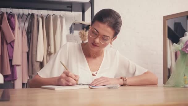 Designer schreibt auf Notizbuch neben Schaufensterpuppe auf Tisch  - Filmmaterial, Video